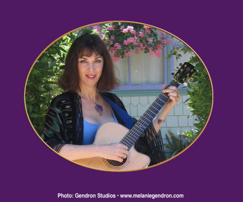 A woman holding a guitar in front of some flowers.